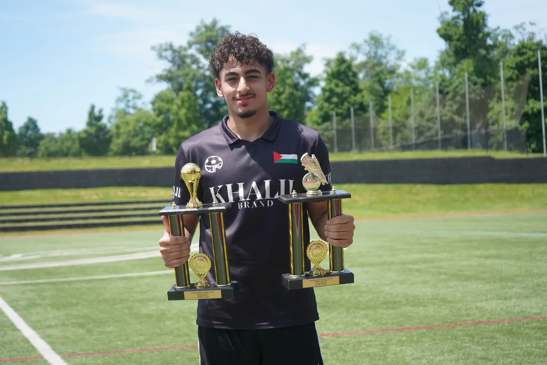 A DMV Muslim League player holding two tournament trophies on the pitch