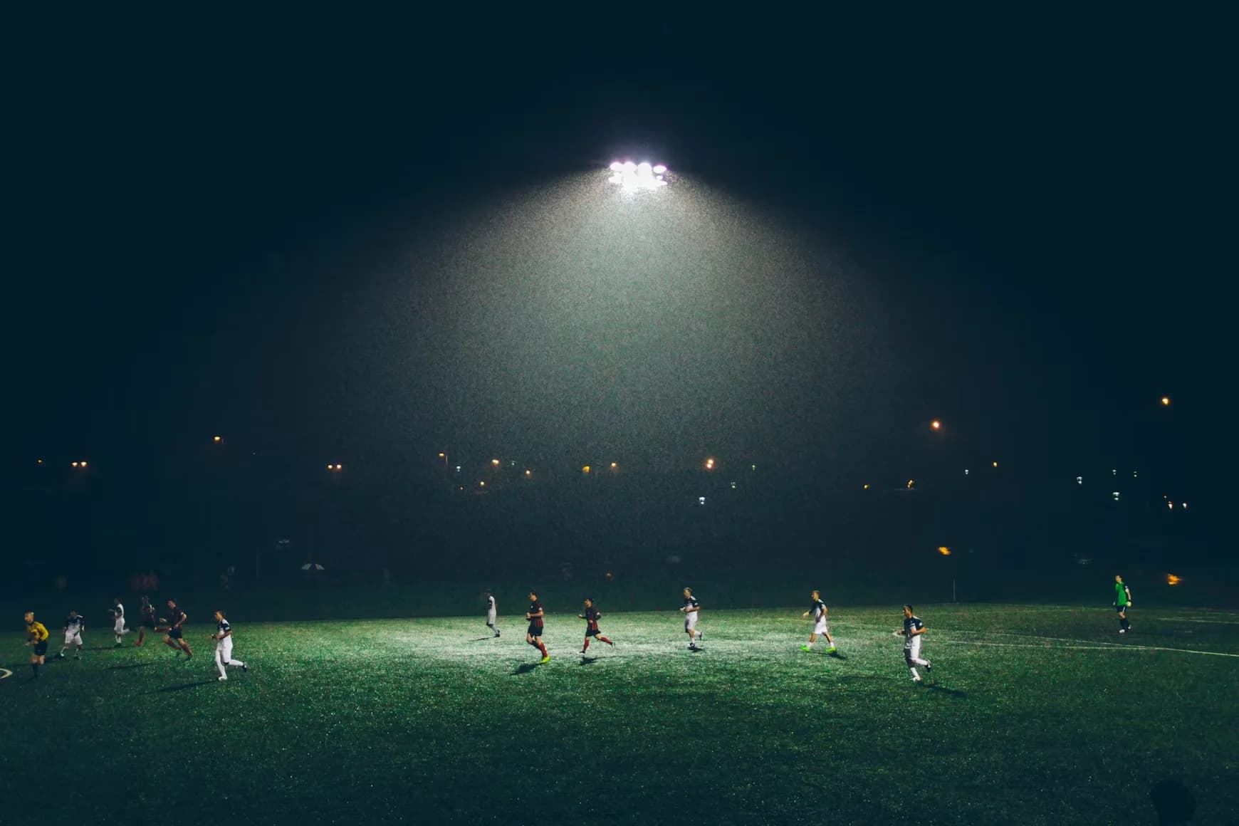 A soccer match under floodlights at night, the beam lighting the pitch as players run